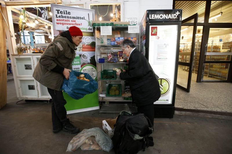 Raphael Fellmer (L), a supporter of the foodsharing movement brings food sorted out from waste bins of an organic supermarket to a distribution point at the indoor market Markthalle Neun (indoor market nine) as a woman takes a piece of bread in Berlin, January 31, 2013. Foodsharing is a German internet based platform where individuals, retailers or producers have the possibility of offering surplus food to consumers for free. Picture taken January 31. TO MATCH STORY GERMANY-FOODSHARING/ REUTERS/Fabrizio Bensch (GERMANY - Tags: FOOD POLITICS SOCIETY)